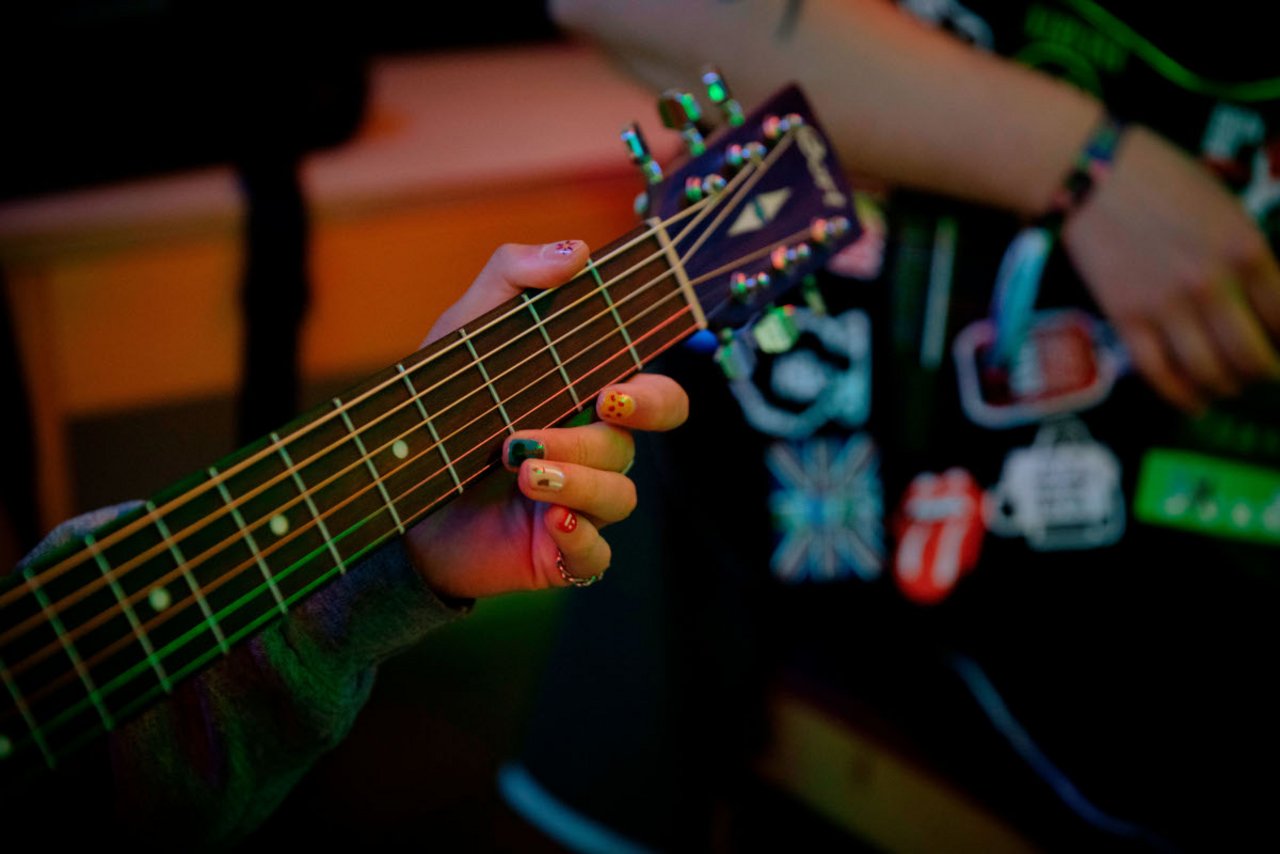 Einblicke ins Seminar: Das Bild zeigt nur den Ausschnitt eines Gitarrenhalses und eine Hand mit buntem Nagellack an jedem Finger am Griffbrett.