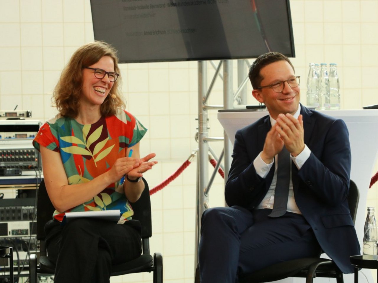 Auf diesem Bild ist der Nieders&auml;chsische Kulturminister Falko Mohrs sitzend abgebildet, der an der Podiumsdiskussion teilgenommen hat. Links neben ihm sitzt Moderatorin Anna Erichson von der LKJ. Beide l&auml;cheln und klatschen. 