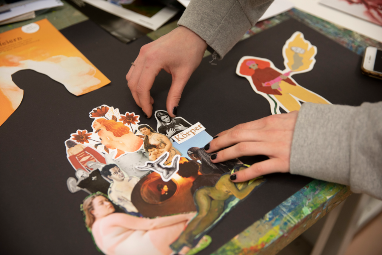 Eindruck aus einem Seminar: Der Bildausschnitt zeigt eine Collage aus Papierausschnitten aus Zeitschriften und eine Paar H&auml;nde, das sie auf einem schwarzen Untergrund positioniert. Der Fokus liegt auf dem Foto einer Frau, die ihre Br&uuml;ste mit beiden H&auml;nden umfasst und darauf hinabschaut. Darunter ist der Schriftzug "K&ouml;rper" platziert. Die Collage zeigt dar&uuml;ber hinaus weitere Fotos und Gem&auml;lde von teils nackten K&ouml;rpern. 