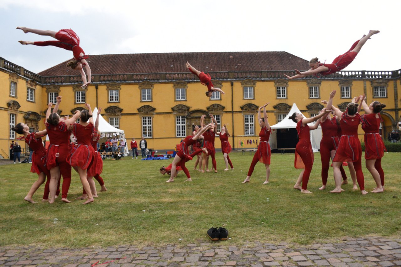 Das Bild zeigt drei Gruppen von Artistinnen der Zirkusgruppe Bikonelli. Sie stehen im Innenhof des Osnabr&uuml;cker Schlosses auf einer Rasenfl&auml;che. Jede Gruppe wirft gerade eine Artistin in die Luft. 